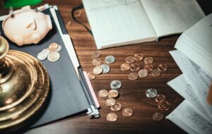 Image of coins scattered on a desk with books scattered around and a piggy bank